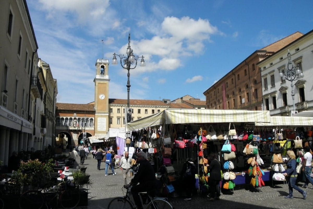 Interno di negozio di biciclette con modelli classici appesi alle pareti, banchi in legno e attrezzi da riparazione, strada di Ferrara sullo sfondo