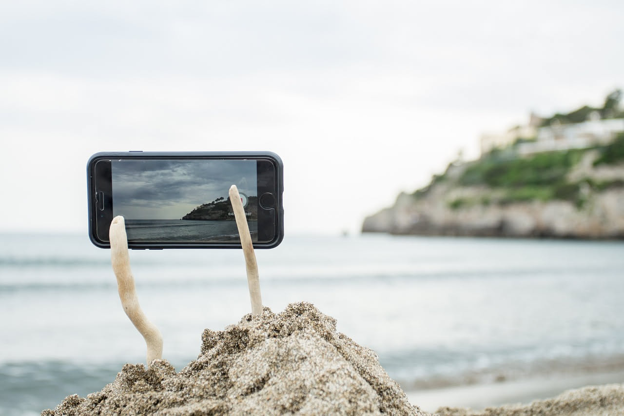 Telefono smartphone con icona di rete spenta e simboli di IA accesi sullo schermo, circondato da immagini di montagna e spiaggia